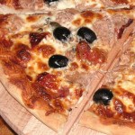 Kawałek pysznej pizzy z tuńczykiem, czarnymi oliwkami, suszonymi pomidorami i kaparami